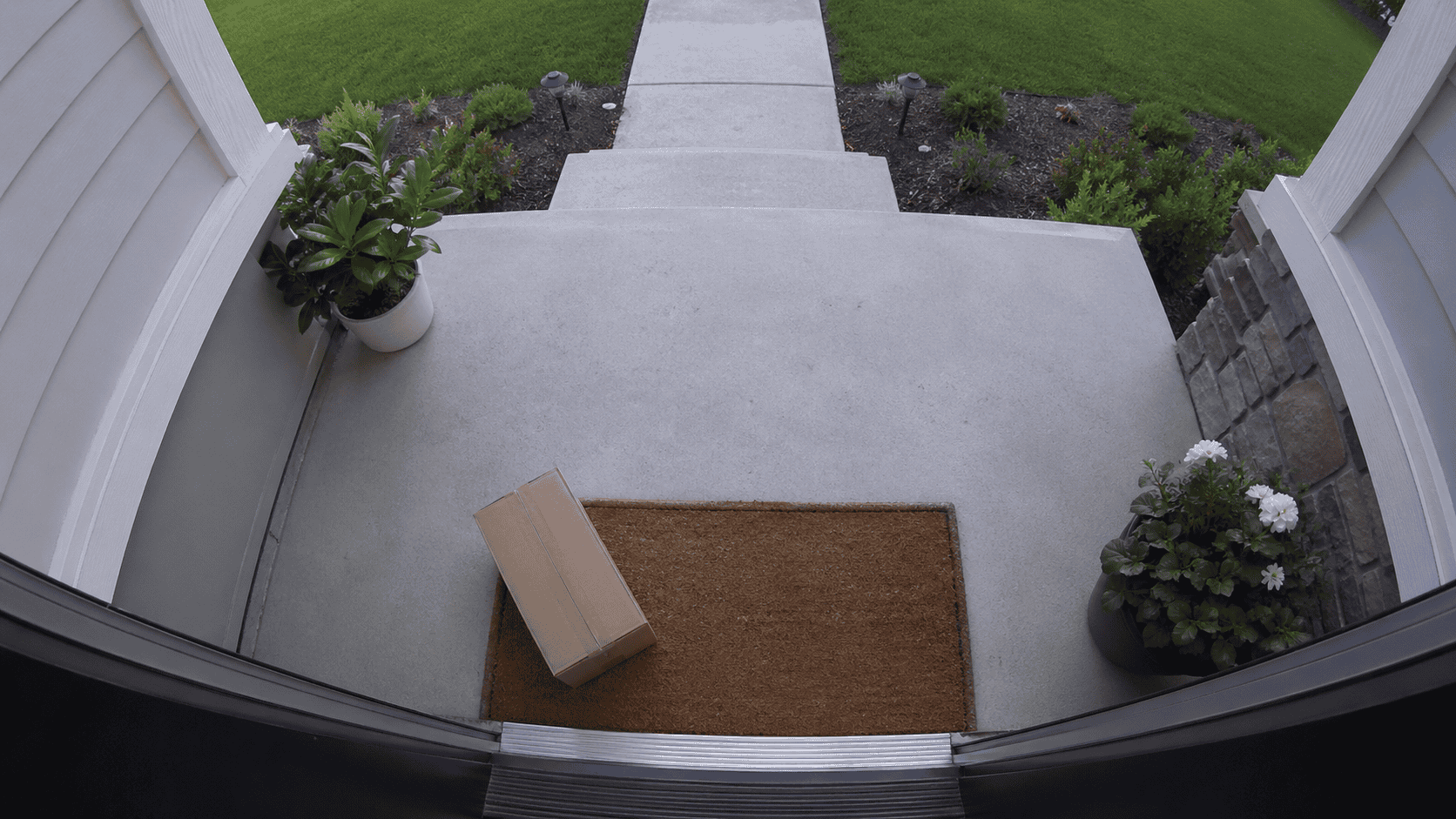 Front porch viewed from a doorbell camera perspective with wide-angle distortion, showing a package on the doormat in daylight.
